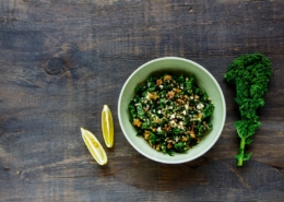 Bowlk of fresh kale and quinoa salad with lime wedges